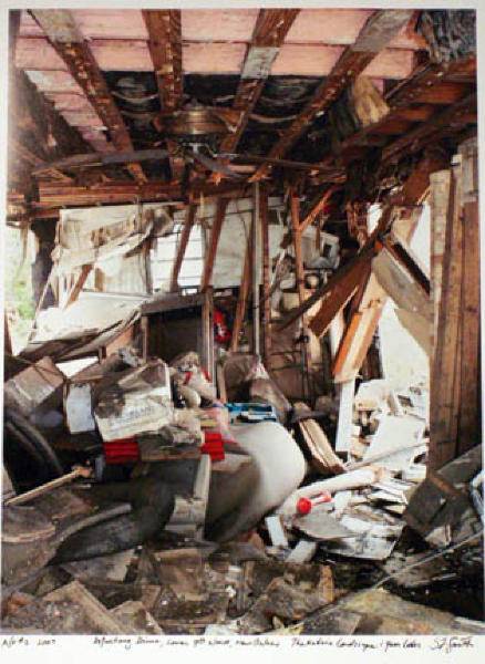 From the series of photographs by Steven L. Smith; image of a gutted house. The walls and ceiling are stripped to the bare studs. Insulation hangs from the open ceiling. There is a lot of refuse in the center of the room including clothes and furniture.